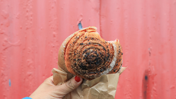 A person holding a cinnamon roll with a red background