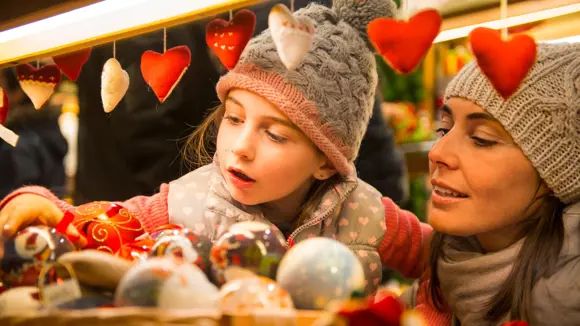 A mother holding her daughter as she looks at decorations at a Christmas market.