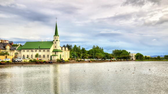A church with a green roof and spire on the shores of Lake Tjornin in Reykjavik.