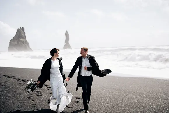 A newly married couple walking along the black sand beach of Vik, Iceland.