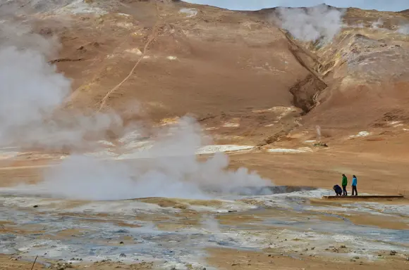 People standing and photographing a steaming crater in Námaskarð Pass.