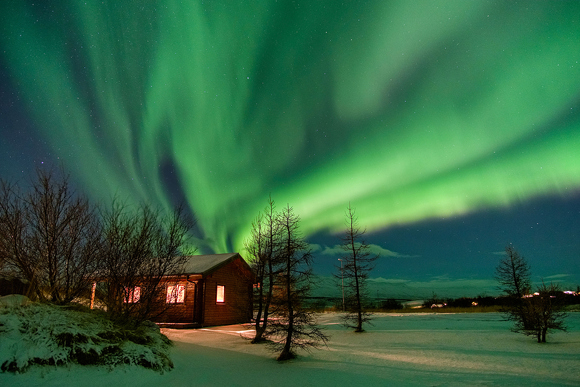 Northern Lights above a remote cottage on a snow-capped landscape in Iceland.