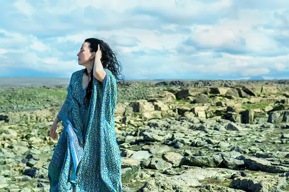 A female model wearing a blue dress with mosaics during a photo shoot at a lava field in West Iceland.