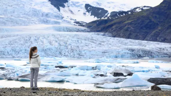 A woman in a lopapeysa standing beside the Vatnajokull glacier in Vatnajokull National Park, Iceland. 