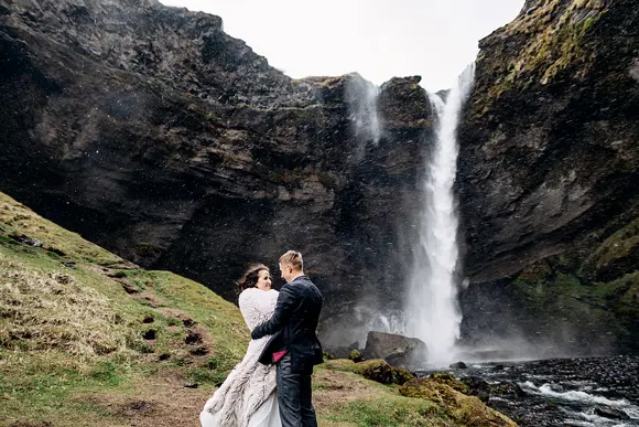 A groom hugging his bride before the Kvernufoss waterfall in Iceland.