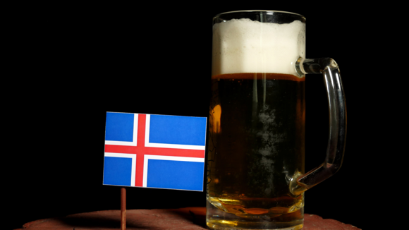 A tankard of frothy beer next to an Icelandic flag on a stick