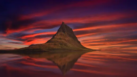 Kirkjufell during a pink sunset with a symmetrical reflection in the lake in the foreground.