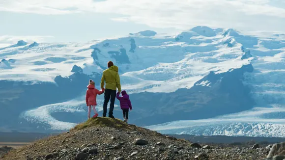 A family standing on a peak and admiring the view of snowy mountains.