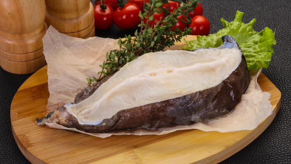 A slice of raw wolffish on a wooden board with other fresh ingredients
