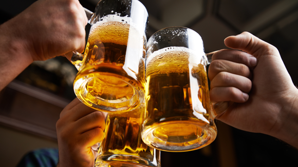 Group of people holding tankards of beer together in a pub.