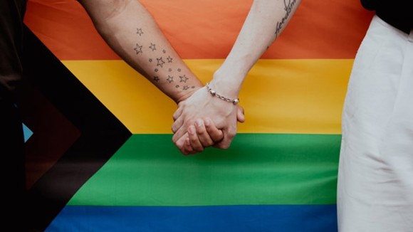 Two people holding hands in front of a pride flag.