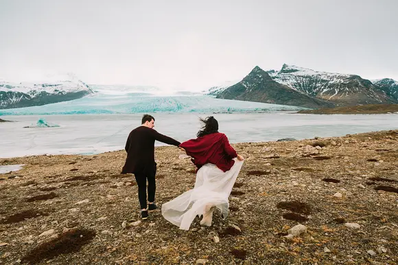 A bride and a groom before a glacial lagoon while getting married in Iceland.