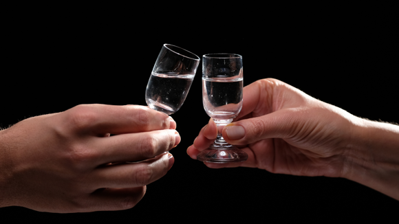 Two hands holding small shot glasses reaching to toast