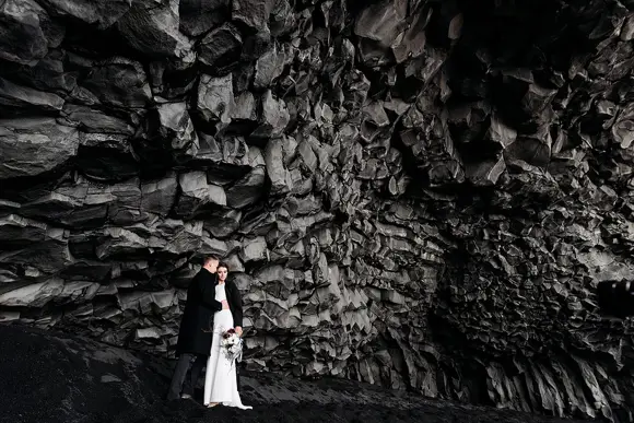 A couple having a destination wedding under basalt rocks near the black sand beach of Vik in Iceland.