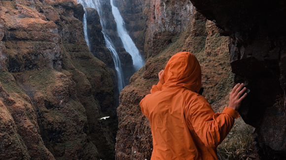 Hiker in an orange waterproof jacket ascending the canyon to Glymur.