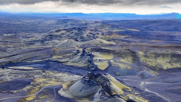 Rolling crater row covered with green moss, with hills in the distance.