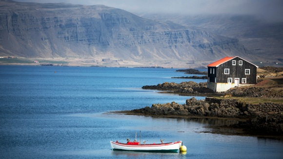 View of a black wooden house and boat on the edge of one of the Eastfjords 